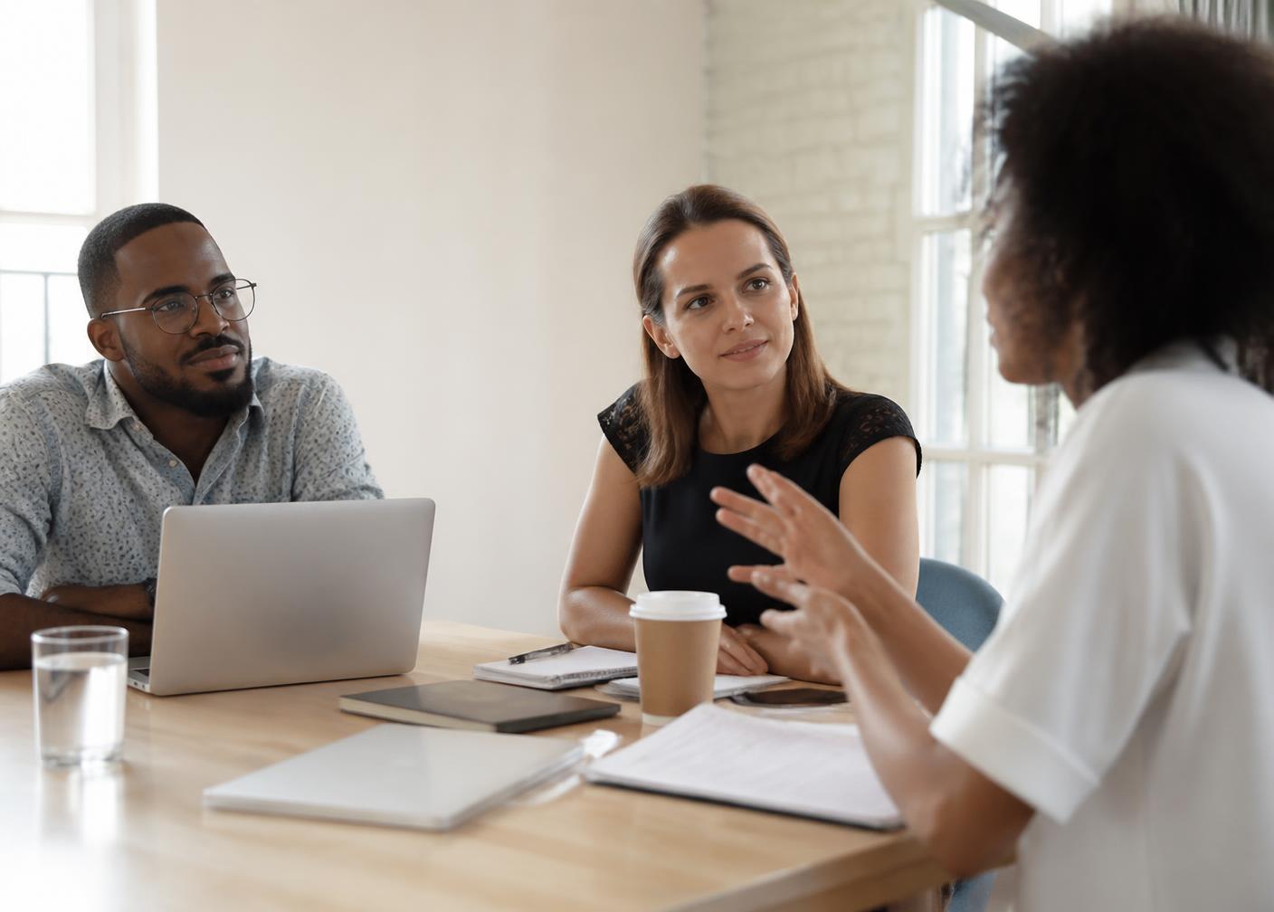 A manager listening attentively to an employee during a small team meeting in a bright office